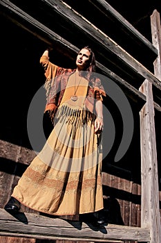 A young woman stands full-length on the porch of the house,