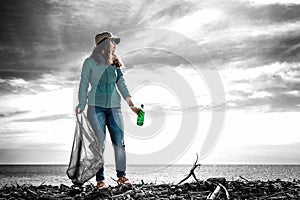 A young woman stands with a garbage bag and a bottle in her hand. Black and white background. Keeping the environment clean . Tint