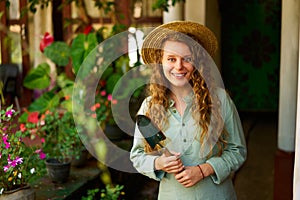 Young woman stands in garden holding gardening tool in her hands smiles and looks at camera. Junior female gardener with