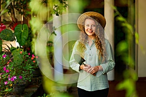 Young woman stands in garden holding gardening tool in her hands smiles and looks at camera. Junior female gardener with