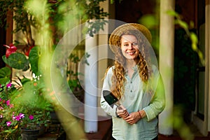 Young woman stands in garden holding gardening tool in her hands smiles and looks at camera. Junior female gardener with