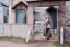 Young woman stands at the gates of a retro medieval church in wild west, America. Vintage clothes on Halloween style 18-19th