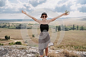 A young woman stands with her hands up in the fresh air in a mountainous area. A smiling woman greets the sun.