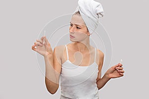 Young woman stands and holds ear sticks in hands. She looks at them and wonderes. Model wer white t-shirt and white