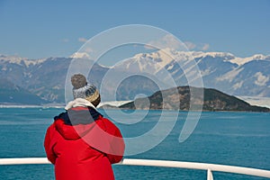 Young woman stands looking at the view from a cruise ship in Alaska