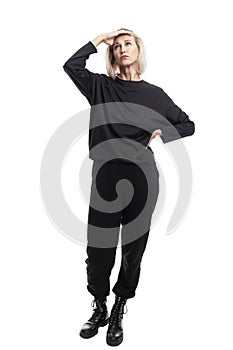 A young woman stands and looks up. Beautiful blonde in a black casual suit. Isolated on white background. Vertical