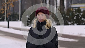 A young woman stands in the middle of the street in winter, waiting for someone. The girl glances at her watch and rubs