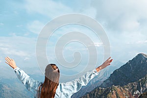 Young woman stands in the mountain with arms outstretched. Freedom and happiness concept with copy space