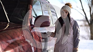 Young woman stands near a car in winter.