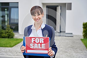 Young woman stands near country house with for sale sign