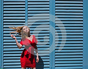 A young woman stands near a wall with blue shutters. Bright sunny day, hard light.The girl develops hair