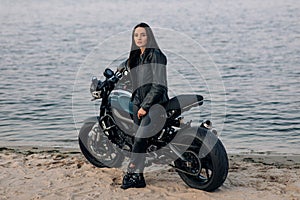 Young woman stands next to motorbike on beach near coast of river