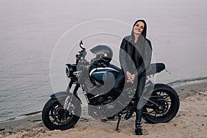 Young woman stands next to motorbike on beach near coast of river