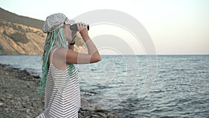 A young woman stands on the shore and looks through binoculars at the sea