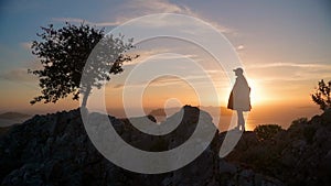 A young woman stands at sunset in the mountains. The silhouette of a girl against the background of the sunset