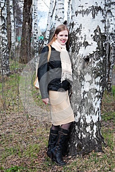 Young woman stands in woods next to birch tree