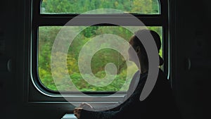 Young woman staring at mountains through train window. Girl traveling by train enjoying nature landscape view from