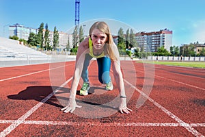 A young woman in the starting position for running on a sports track
