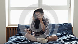 Young woman stay at home during quarantine. Girl sit on bed and afraid to watch movie. Eating popcorn and switch tv