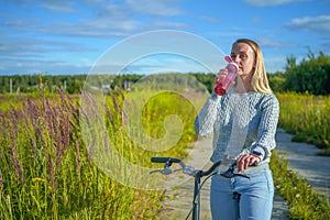 Young woman staying with bicycle and drinking water