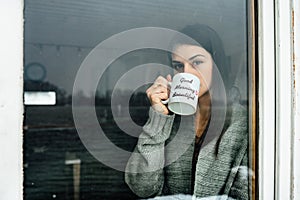 Young woman staying at home drinking coffee/tea,looking trough the window.Starting the day,morning ritual.Quaratine self isolation