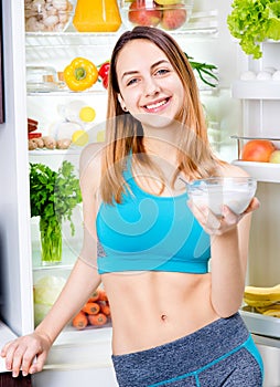 Young woman staying near the fridge full of health food.