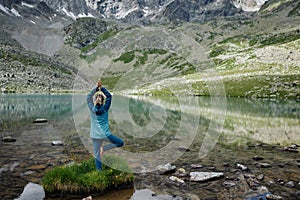 Young woman stays in one leg yoga position against the turquoise lake in the mountains