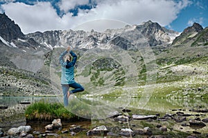 Young woman stays in one leg yoga position against the turquoise lake in the mountains