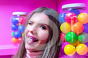 Young woman sticking out her tongue on pink background with colorful balls