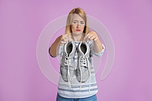 Young woman with stinky shoes on color background