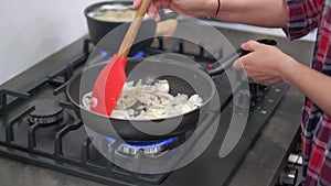 Young woman stirring fried onions in hot pan