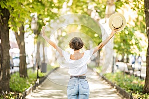 Young woman with straaw hat arms raised enjoying the fresh air in green forest