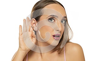 Young woman is straining a hand behind her ear while listening