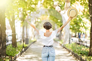 Young woman with straw hat arms raised enjoying the fresh air in green forest