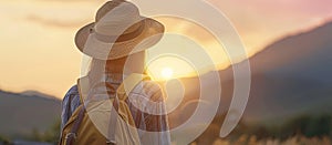 Young woman in straw hat with backpack, admiring sunset over mountains, rear view, travel concept