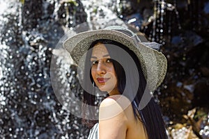 Young woman with straw hat in the forest near the streaming water