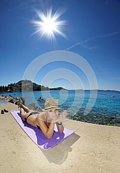 Young woman in straw hat sunbathing on a beach