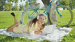 Young woman in straw hat watching laptop on green meadow