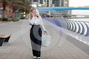 Young woman at the street with shopping bags talking on mobile phone