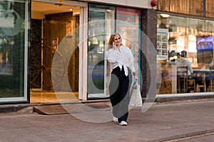 A young woman on the street with shopping bags talking on a mobile phone