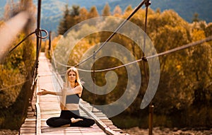 Young woman stretching arms and doing yoga exercises on bridge over river