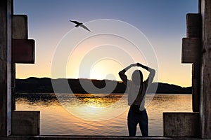 Young woman stretching arms under the sunrise at lake with wooden framing