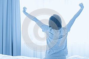 Young woman stretching in bed after wake up, back view