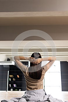 Young Woman stretching in bed after waking up, back view