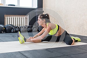 Young woman stretching hamstring in gym, fit female doing warm-up on mat