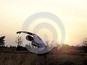 Young woman stretching her arms on beautiful bright sunset sky background near summer field.