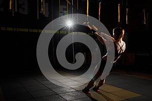 Young woman stretching her body while doing fitness TRX training exercises at gym