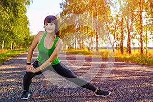 Young woman stretching legs before jogging on asphalt road in countryside