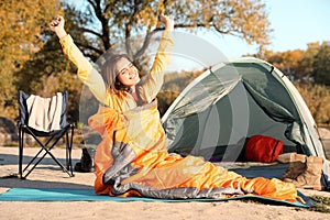 Young woman stretching in sleeping bag near camping tent