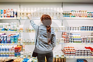 Young woman in striped shirt from back choosing dairy products in supermarket